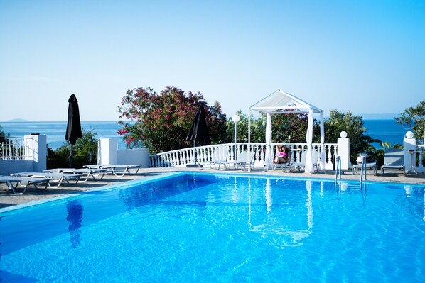 A clear blue pool with lounge chairs and a gazebo overlooking the sea.
