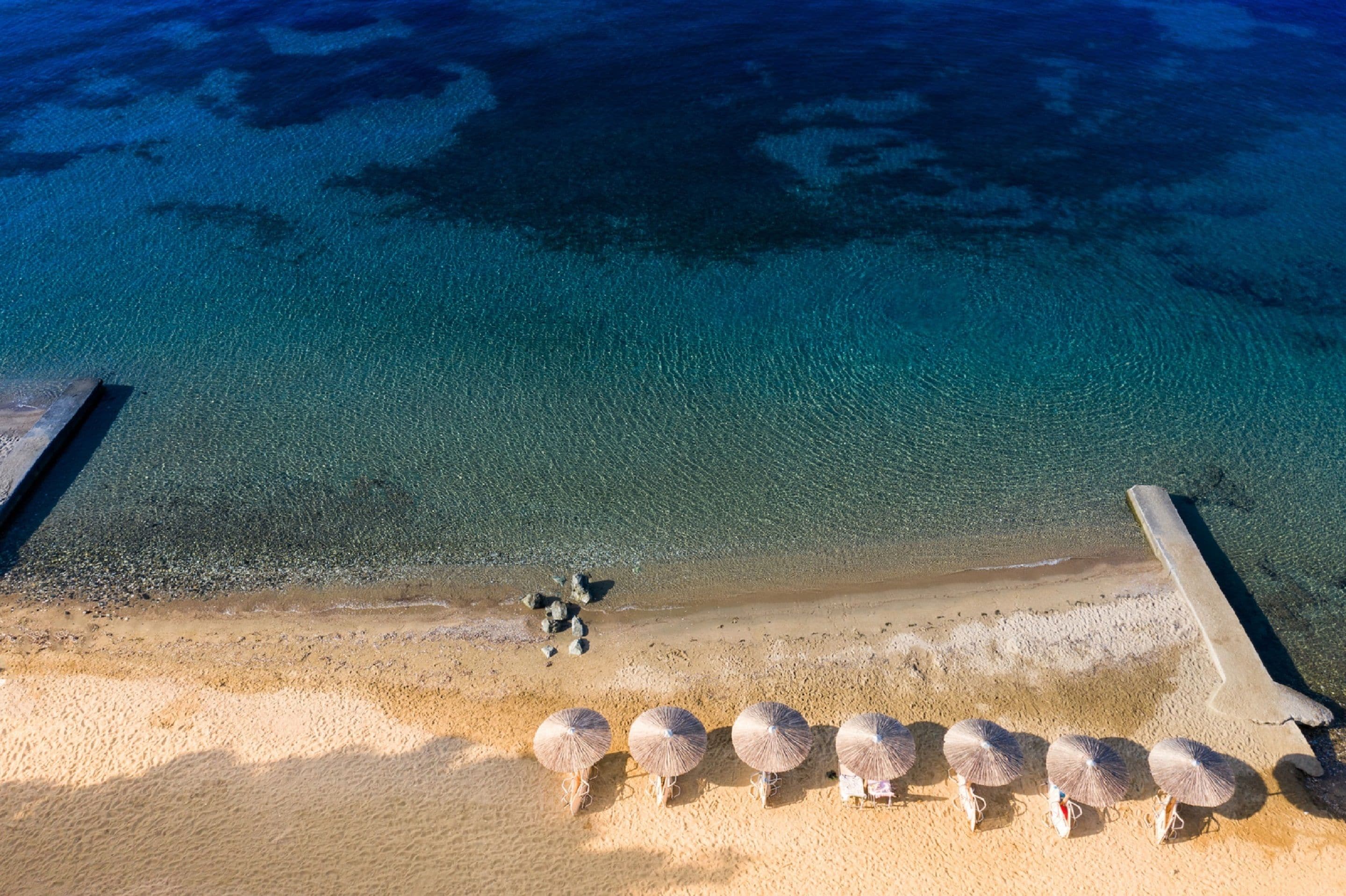 Vista aérea de una playa con agua azul cristalina, una orilla arenosa y varias sombrillas.