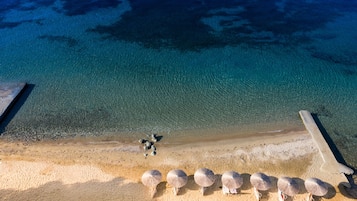 Een luchtendbeeld van een strand met helderblauw water, een zandstrand en verschillende parasols.