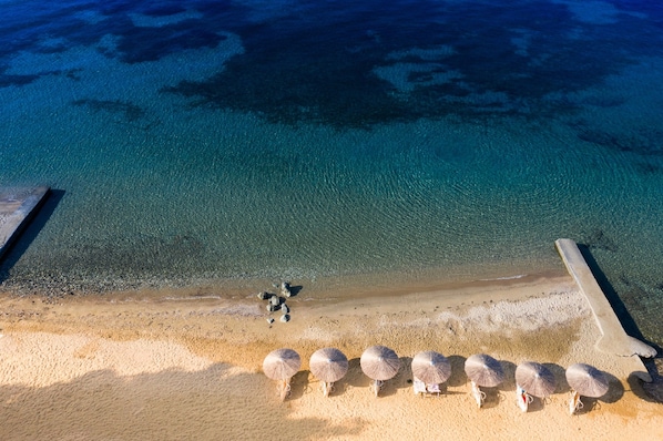 An aerial view of a beach with clear blue water, a sandy shore, and several umbrellas.