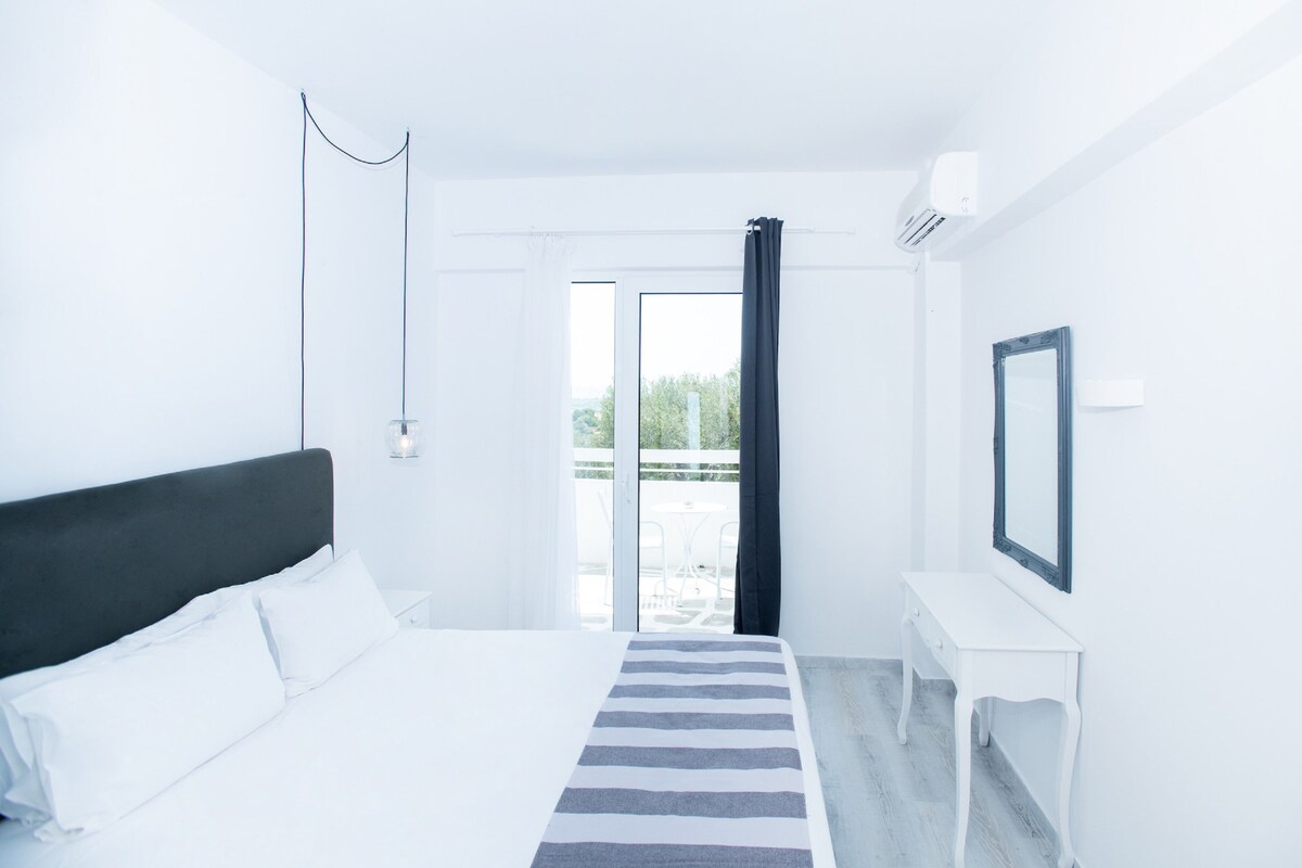 Habitación de hotel con cama, mesita de noche, espejo y vistas al exterior.
