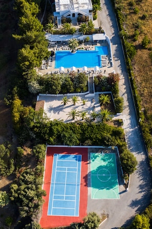 An aerial view of a property with a swimming pool, tennis courts, and a landscaped garden.