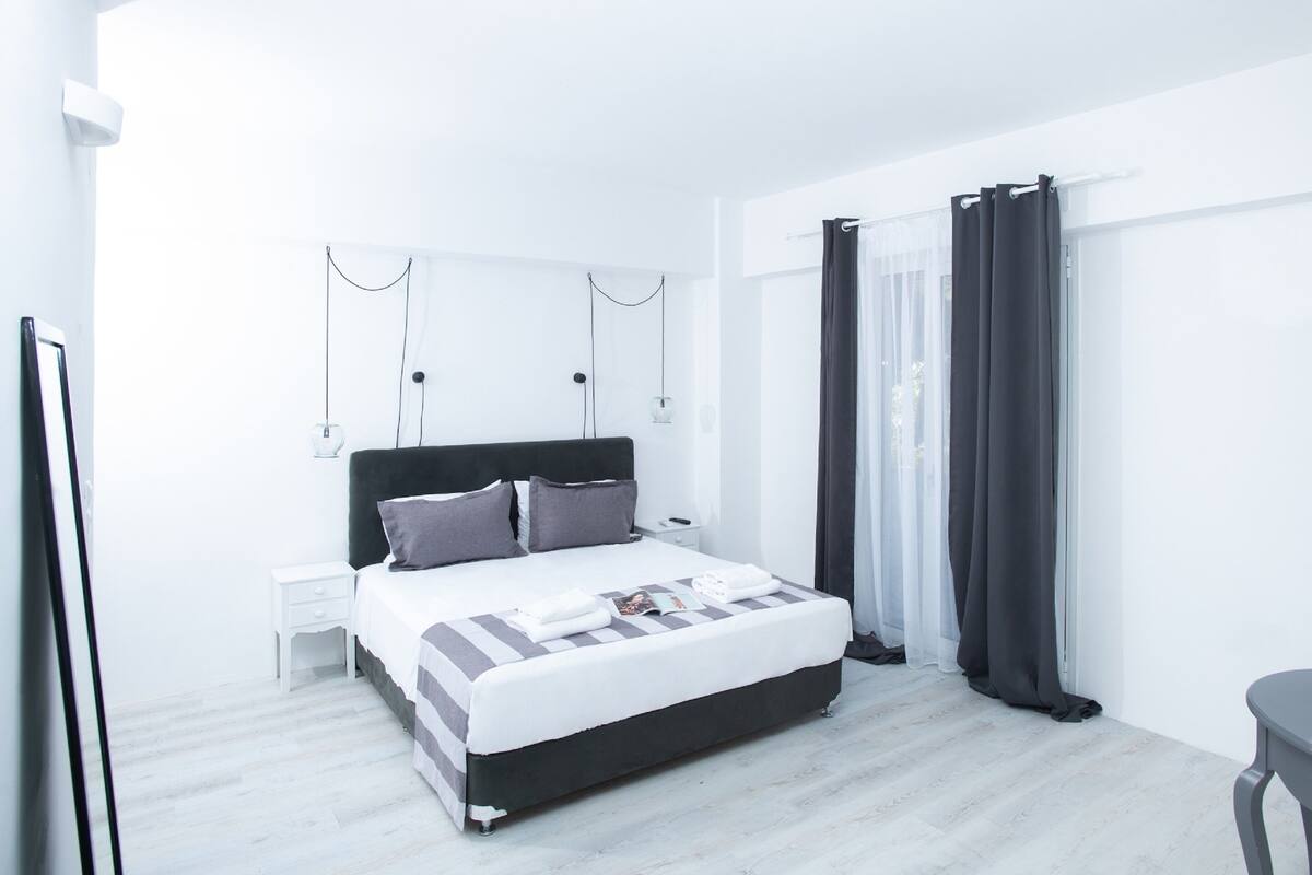 Une chambre moderne avec un grand lit, une table de chevet et une fenêtre avec des rideaux.