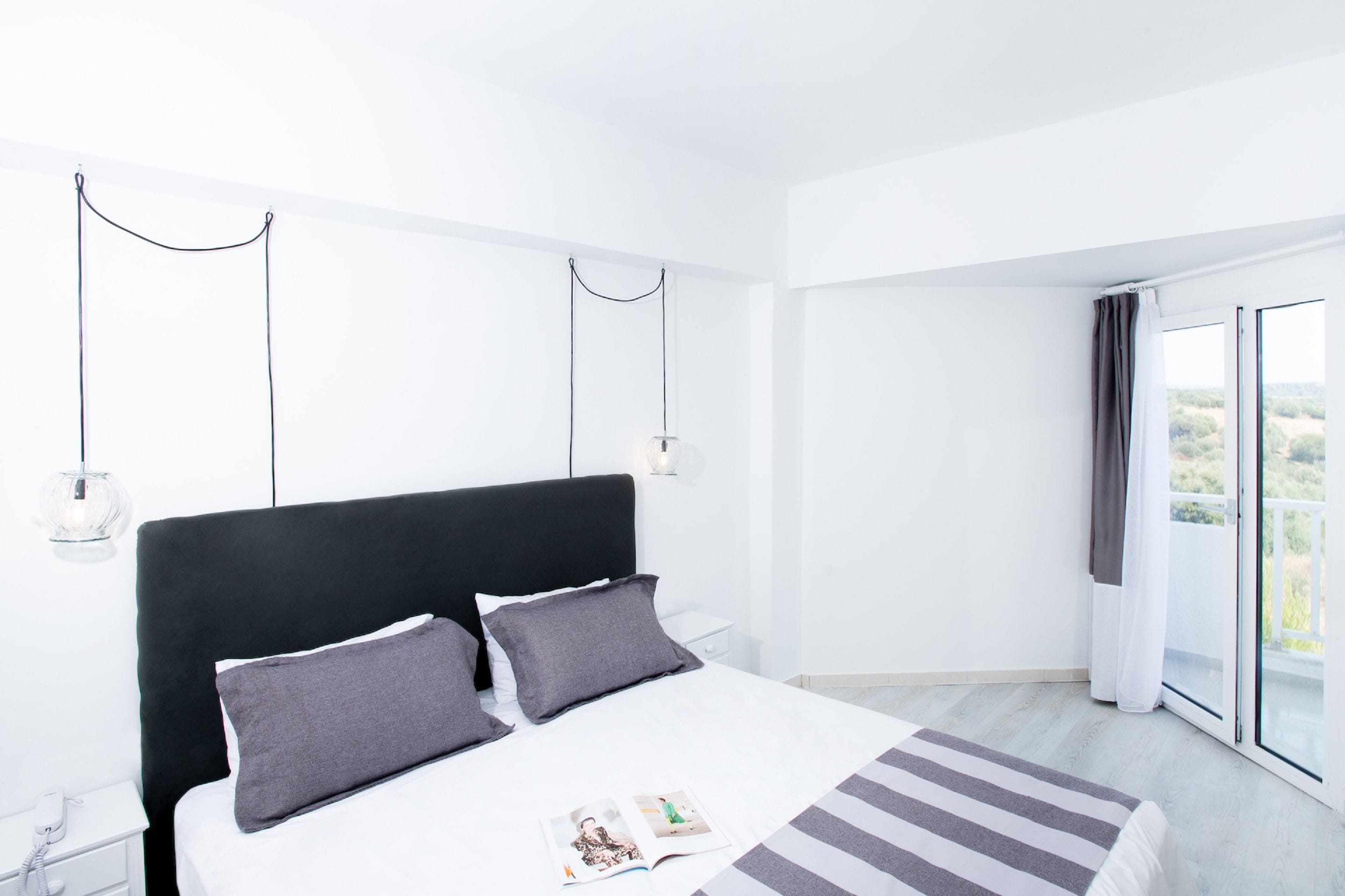 Una habitación de hotel moderna con una cama grande, una mesita de noche, una lámpara y vistas al exterior.