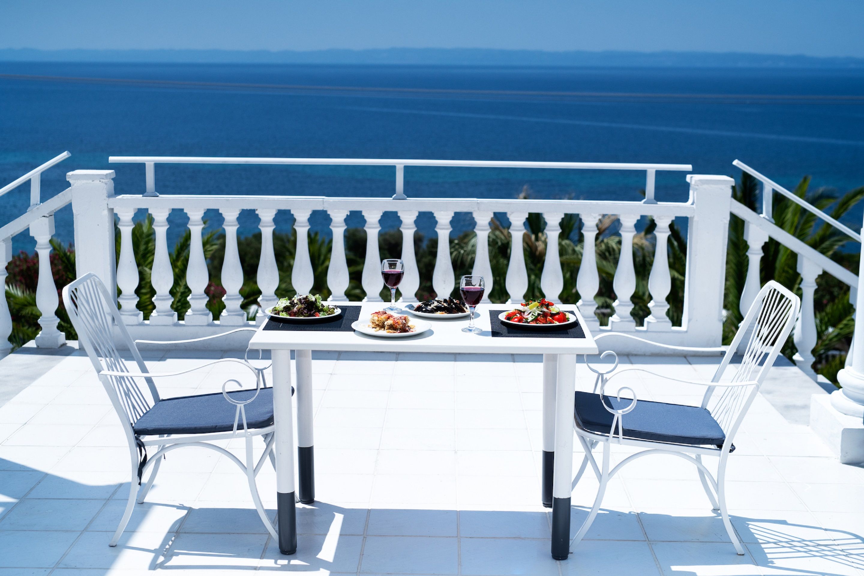 Mesa para dos con platos de comida y copas de vino, con vistas a la costa.