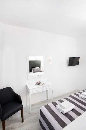 A minimalist hotel room with a bed, a white desk, a black chair, a flat-screen TV, and a mirror. - Bianco Olympico Beach Resort By Anayia AI Resorts (Polygyros)
