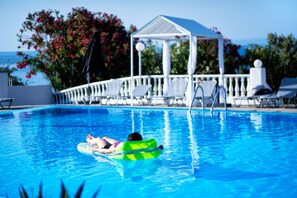 A swimming pool with a person on a green float, lounge chairs, and a gazebo in the background. - Bianco Olympico Beach Resort By Anayia AI Resorts (Polygyros)