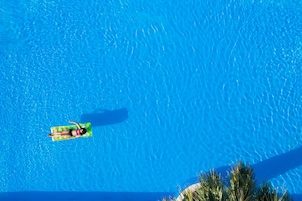 Una piscina azul cristalina con una persona flotando sobre una boya verde hinchable.