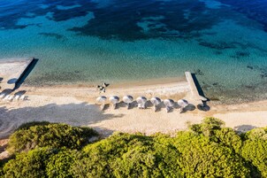 An aerial view of a beach with clear blue water, a sandy shore, and a row of umbrellas.
