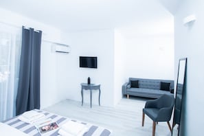 A modern hotel room with a bed, a grey sofa, a small table, and a TV mounted on the wall.