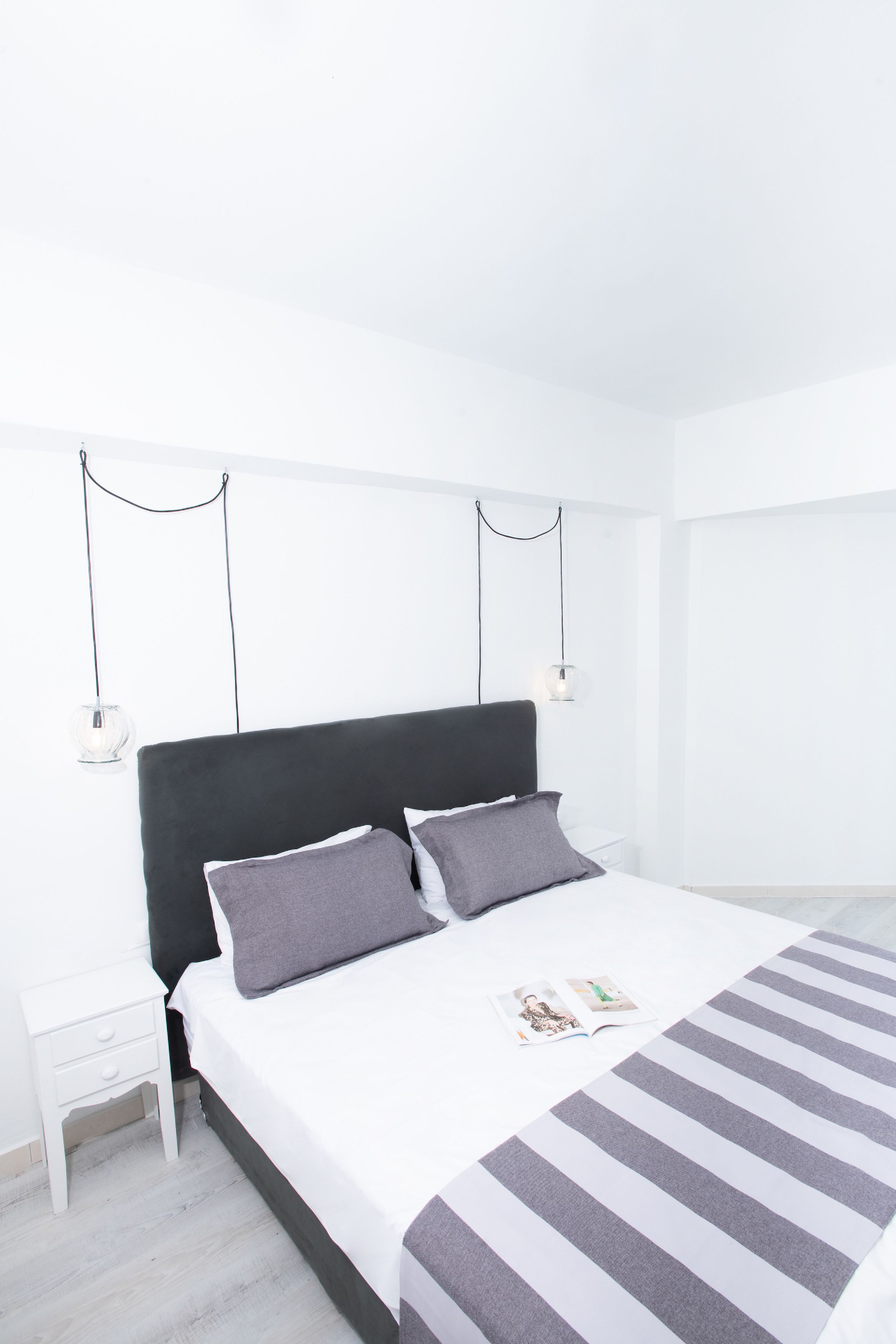 A minimalist bedroom with a large bed, two bedside tables, and a hanging light fixture.