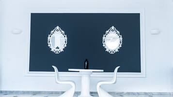 A room with a dark blue accent wall, two ornate white mirrors, a white table with a black bottle, and white chairs.