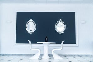 A room with a dark blue accent wall, two ornate white mirrors, a white table with a black bottle, and white chairs. - Bianco Olympico Beach Resort By Anayia AI Resorts (Polygyros)