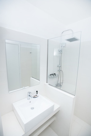Une salle de bain moderne avec un lavabo blanc, un grand miroir et une douche à parois de verre.