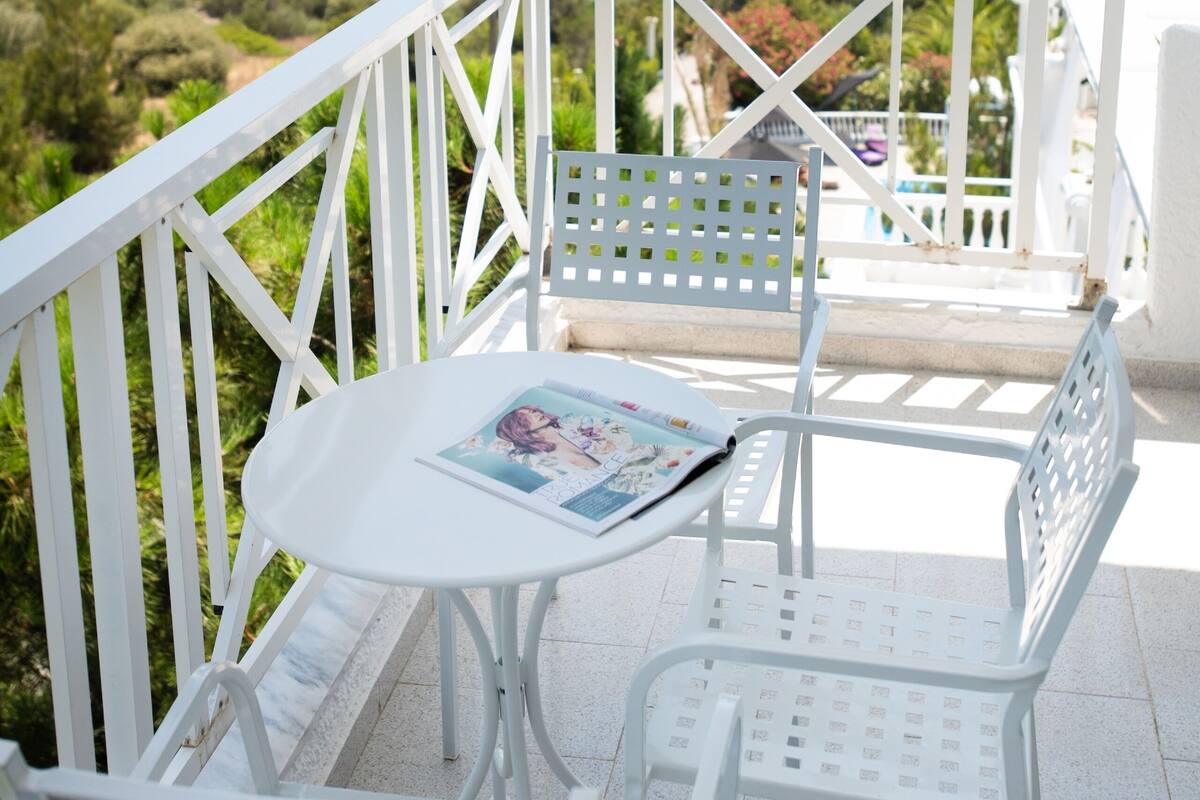 A balcony with white metal railings, a small round table, and two white metal chairs.