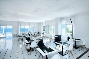 A modern, well-lit conference room with a panoramic sea view, featuring a clean layout with tables and chairs.