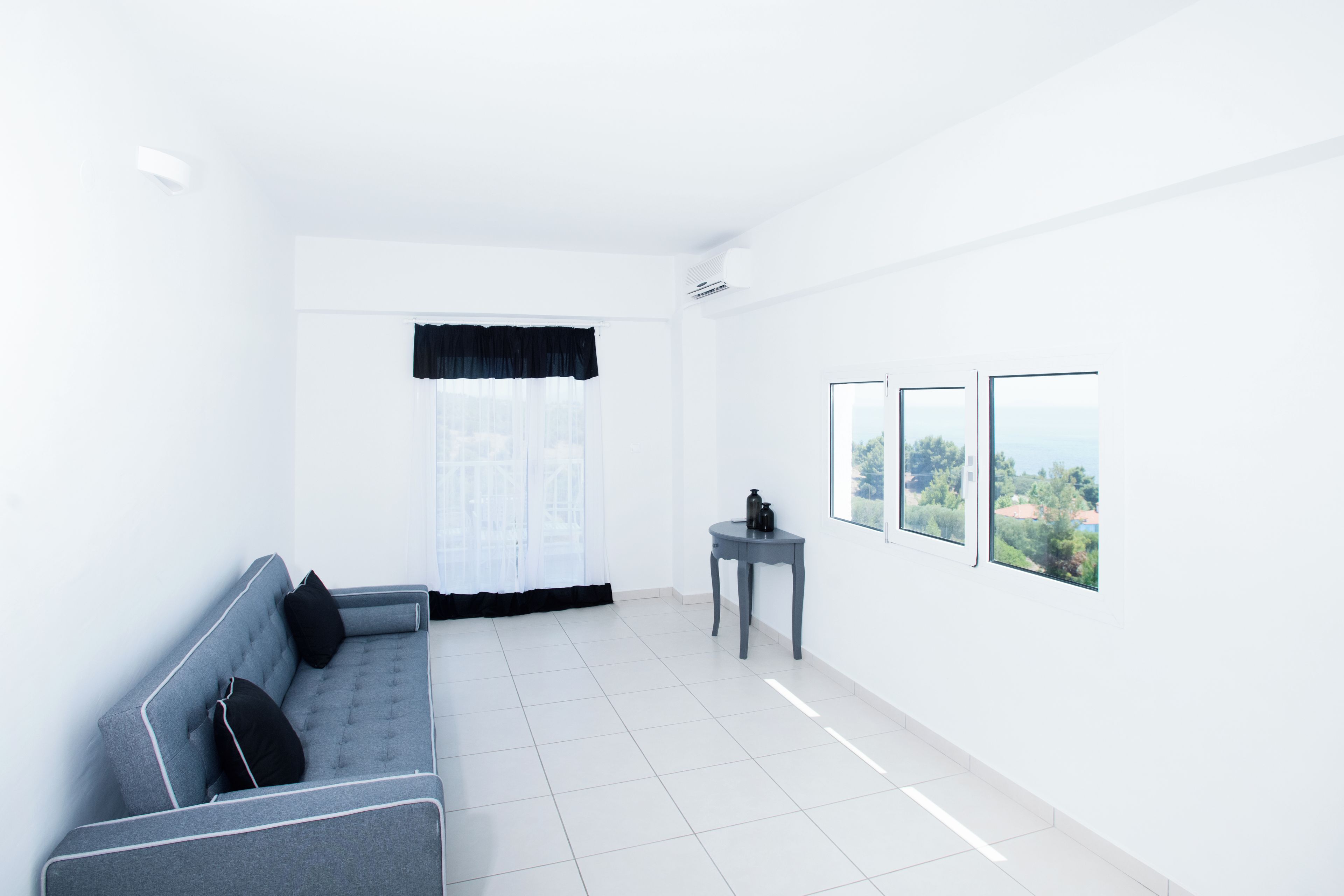 A minimalist living room with a grey sofa, a small side table, and a view of greenery through the window.