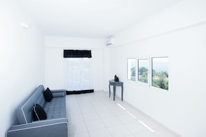 A minimalist living room with a grey sofa, a small side table, and a view of greenery through the window.