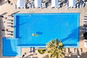 Piscina rectangular con una persona flotando en un inflable, rodeada de sillas de descanso y sombrillas.