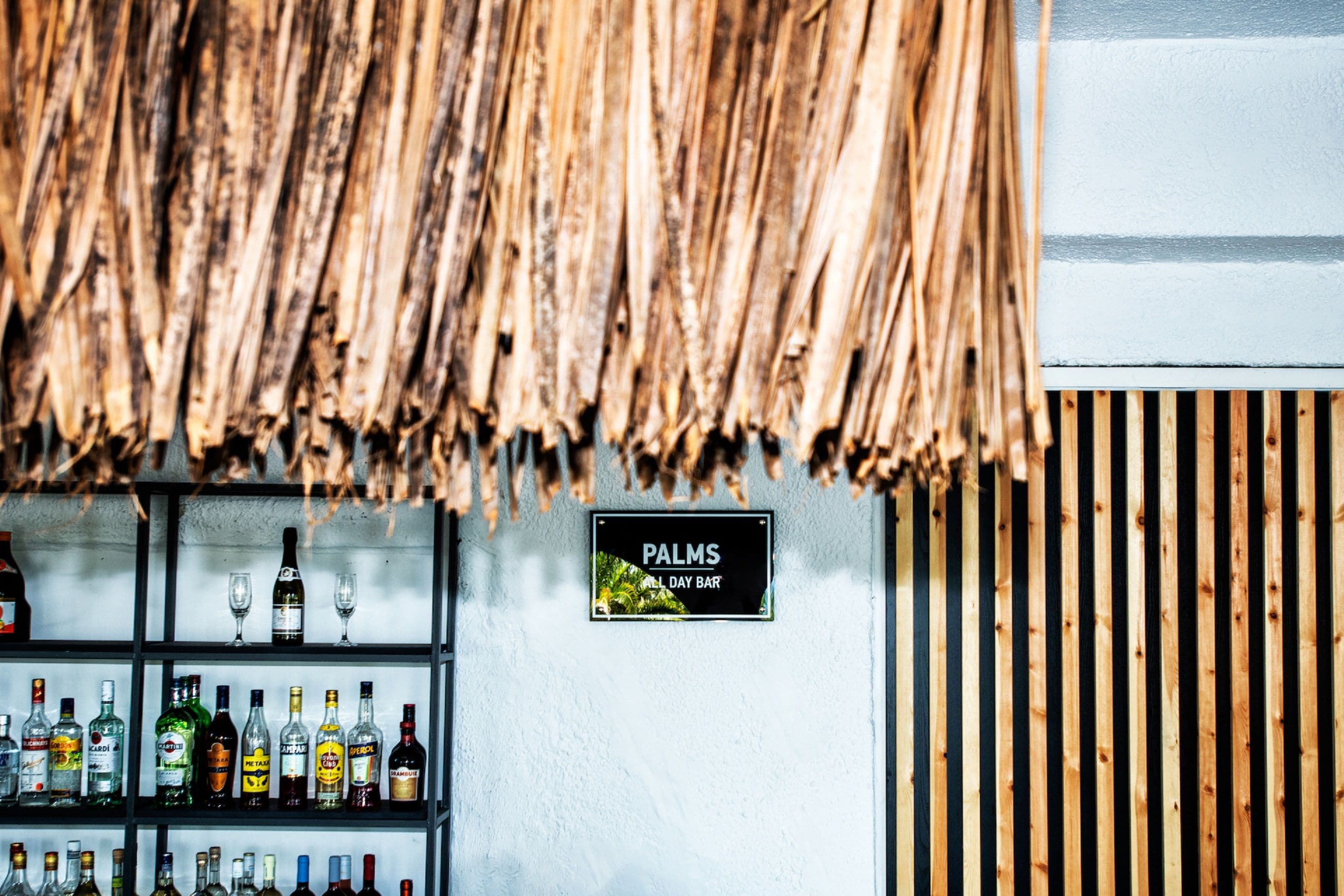 Eine Bar mit einer Schilder 'PALMS ALL DAY BAR' und Regalen voller verschiedener Spirituosenflaschen.