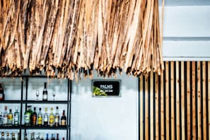 Zona de bar con un letrero que dice 'PALMS ALL DAY BAR' y estantes llenos de diferentes botellas de licor.