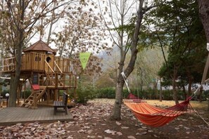 A wooden playhouse with a slide, a hammock, and a picnic table in a wooded area. - Kensington Resort Gapyeong (Gapyeong-gun)