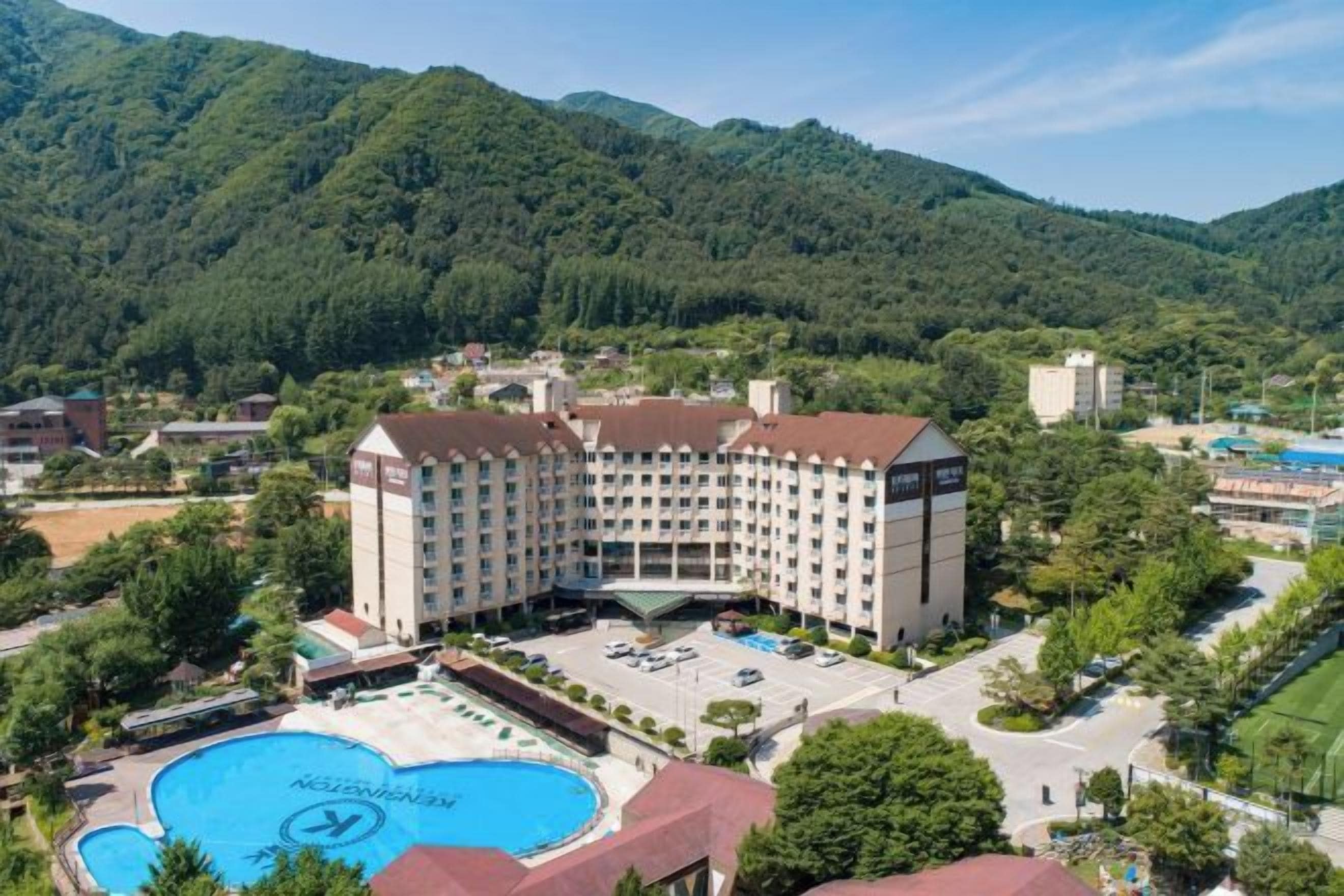 A hotel with a swimming pool, surrounded by lush greenery and mountains.