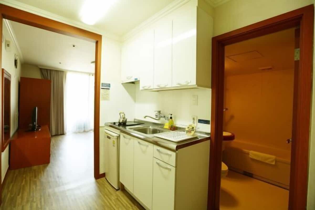 A compact hotel room with a kitchenette, a bathroom, and a wooden floor.