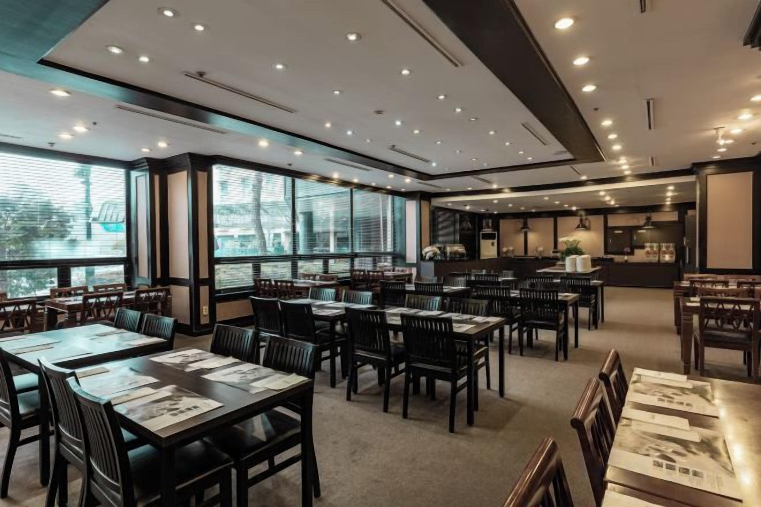 A restaurant with multiple tables and chairs, large windows, and a kitchen area.