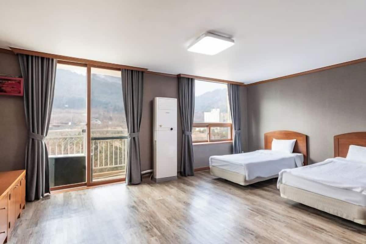 A hotel room with two beds, a wardrobe, a desk, and a balcony with a view of mountains.