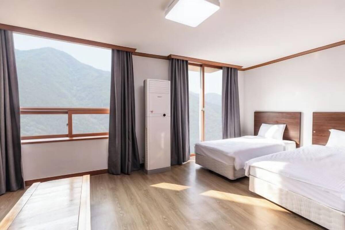 A hotel room with two beds, a refrigerator, and a view of mountains.