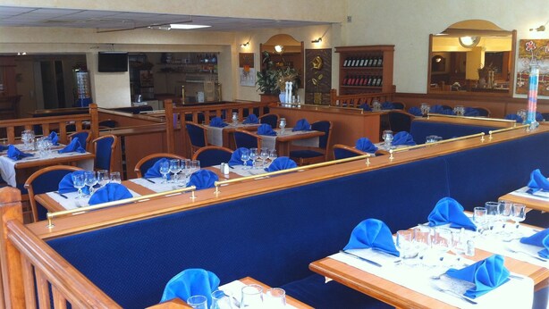 A restaurant with booths and tables, each set with blue napkins and clear glasses. - Hotel Le Mejean (Lattes)