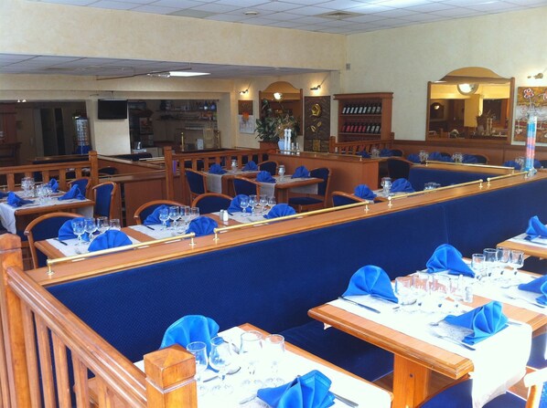 A restaurant with booths and tables, each set with blue napkins and clear glasses. - Hotel Le Mejean (Lattes)