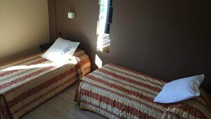 A room with two beds, each with striped bedding and pillows. There is a small window with blinds, and a wall-mounted light fixture. - Hotel Le Mejean (Lattes)