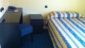 A small hotel room with a desk, a chair, a bed with striped bedding, and a nightstand. - Hotel Le Mejean (Lattes)