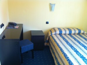 A small hotel room with a desk, a chair, a bed with striped bedding, and a nightstand. - Hotel Le Mejean (Lattes)