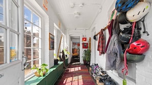 A narrow hallway with a red patterned rug, white walls, and a row of helmets and gear on the right. - Bunk+Brew Historic Lucas House - Hostel (Bend)