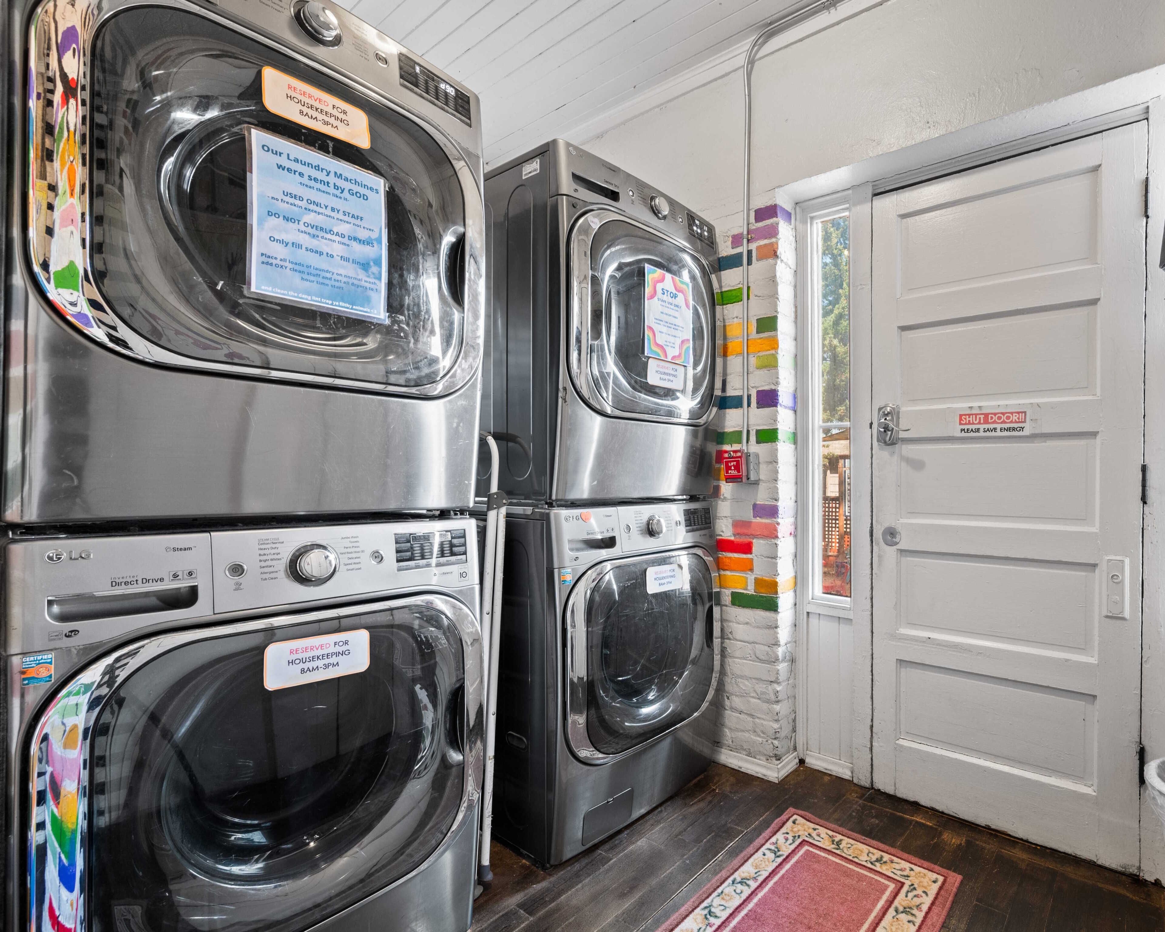 Een wasruimte met gestapelde wasmachines, een deur met een 'STOP'-bord en een kleurrijke bakstenen muur.