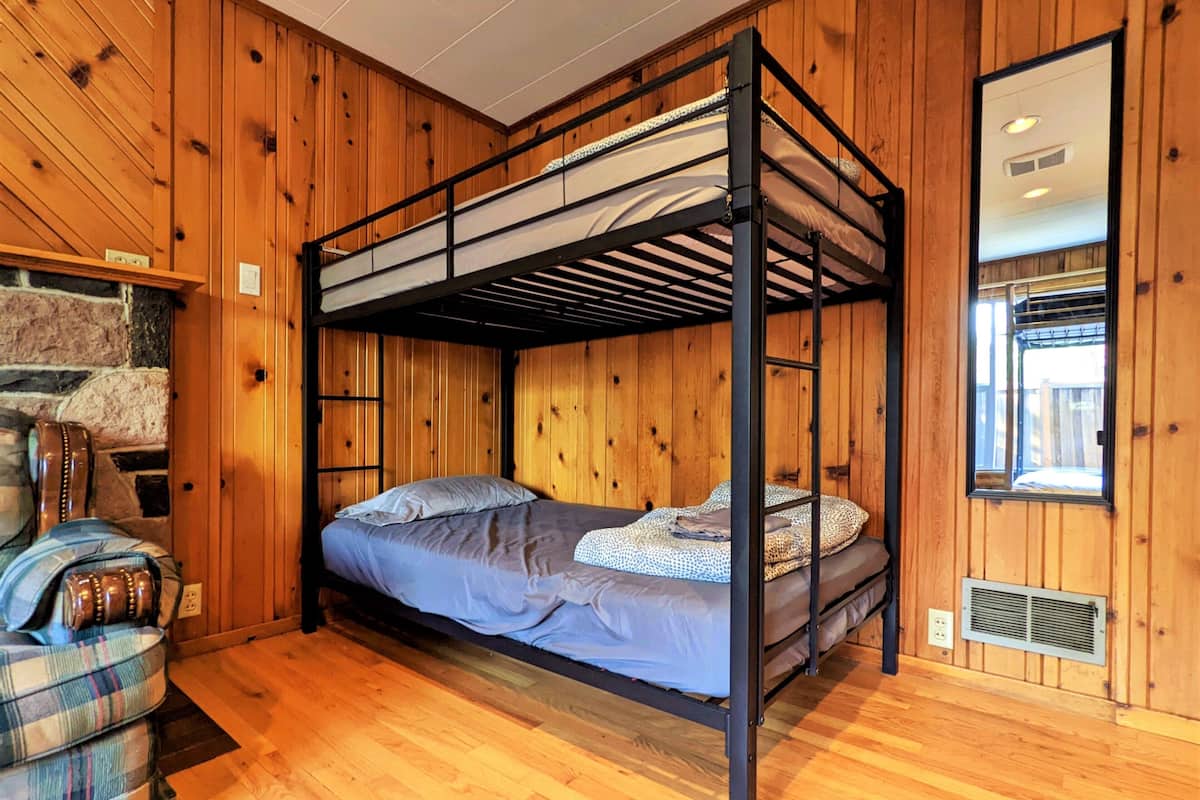 A bunk bed room with wooden walls, a stone fireplace, and a window with a view.