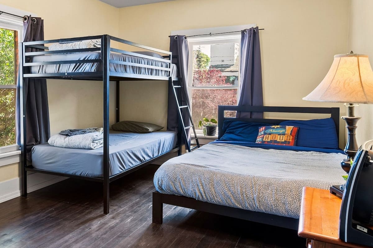 A room with two bunk beds, a wooden nightstand with a lamp, and a window with curtains.