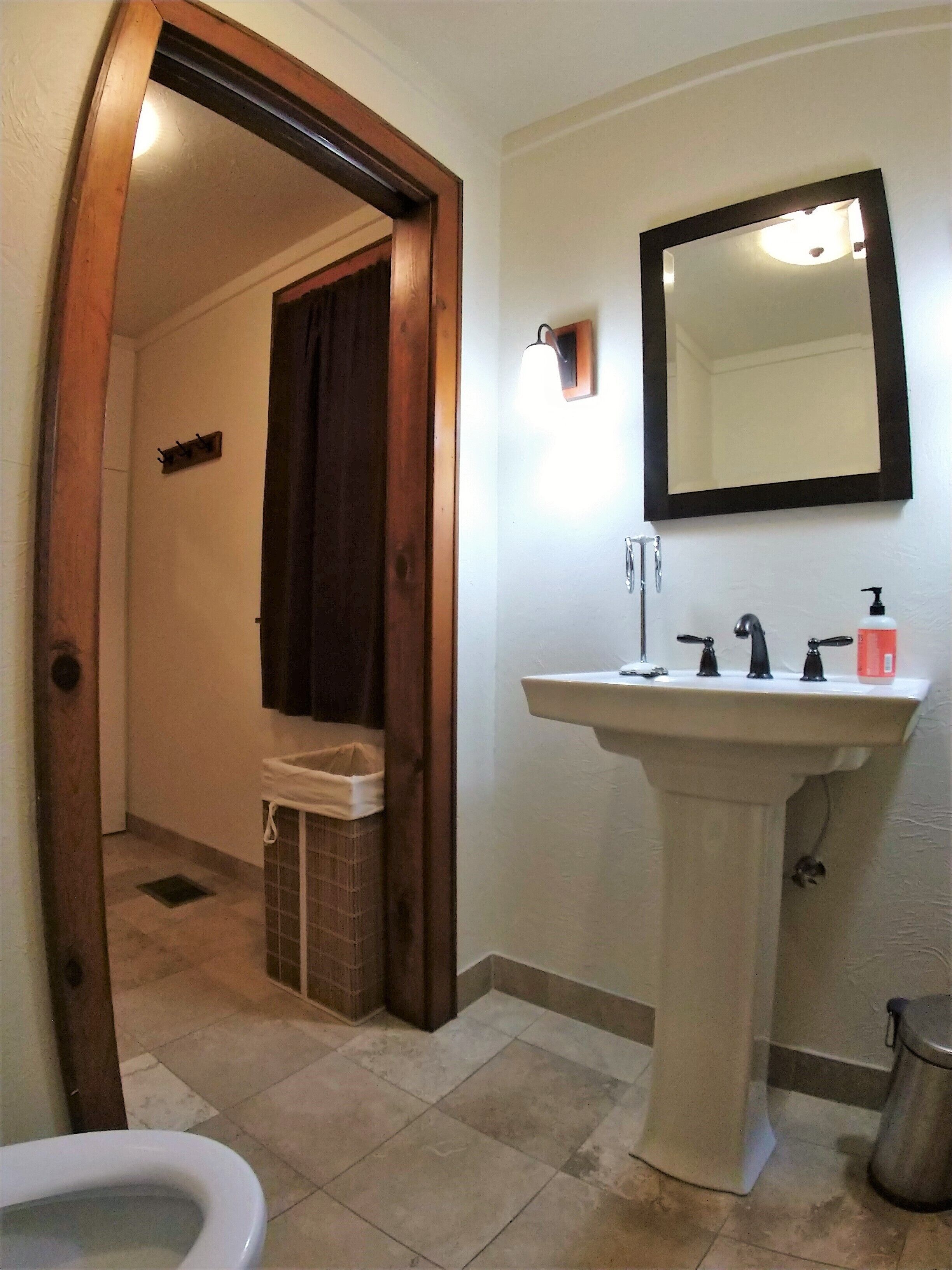 A bathroom with a pedestal sink, a mirror, a toilet, and a shower area.