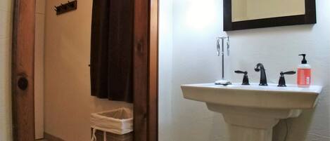 A bathroom with a pedestal sink, a mirror, a toilet, and a shower area.