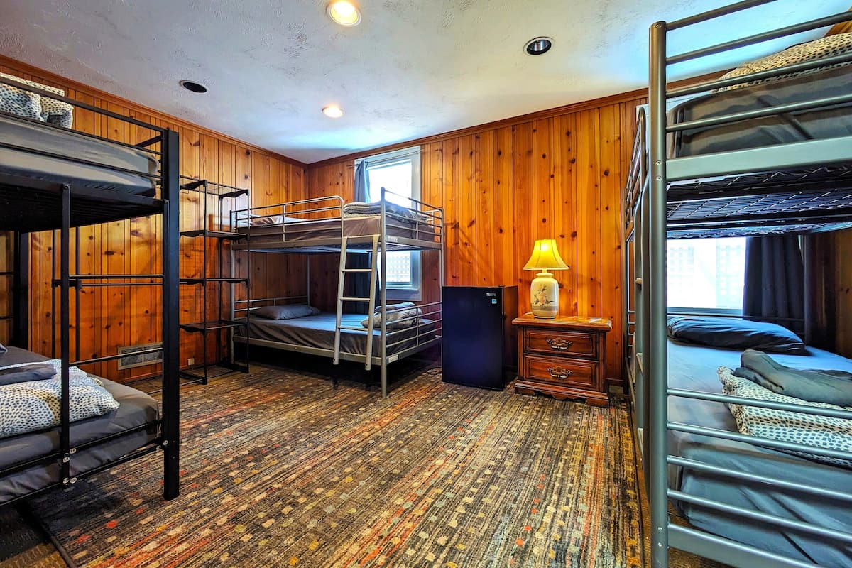 A bunk bed room with wooden walls, a patterned carpet, and a small table with a lamp.
