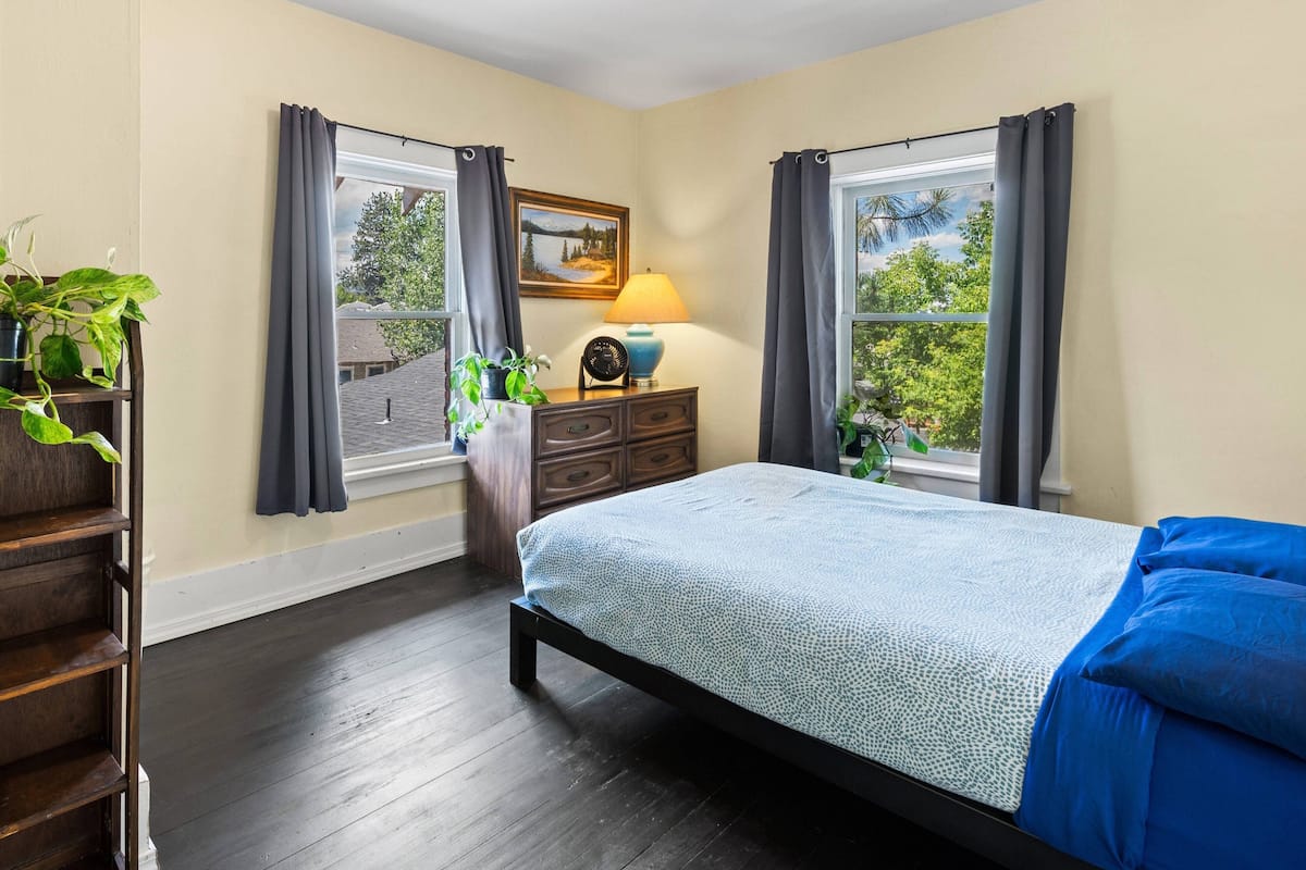 A bedroom with a bed, a dresser, a lamp, and a window with curtains.