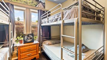Habitación tipo dormitorio con literas, un aparador de madera, un ventilador y una ventana con vistas a la vegetación.