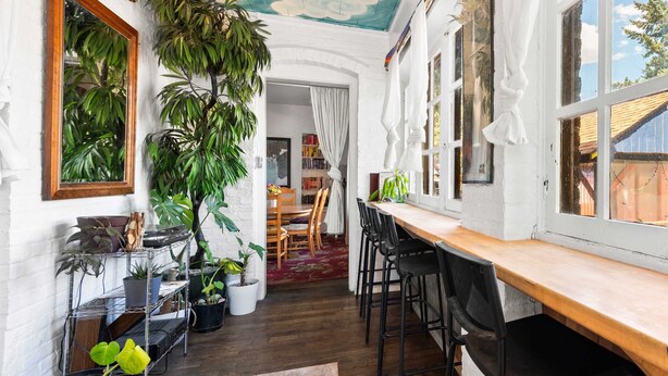 A cozy room with a wooden table, chairs, and a ceiling mural. There are potted plants and a bookshelf. - Bunk+Brew Historic Lucas House - Hostel (Bend)