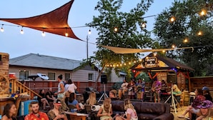 An outdoor gathering with a band performing under a canopy, surrounded by seated guests on sofas and chairs. - Bunk+Brew Historic Lucas House - Hostel (Bend)