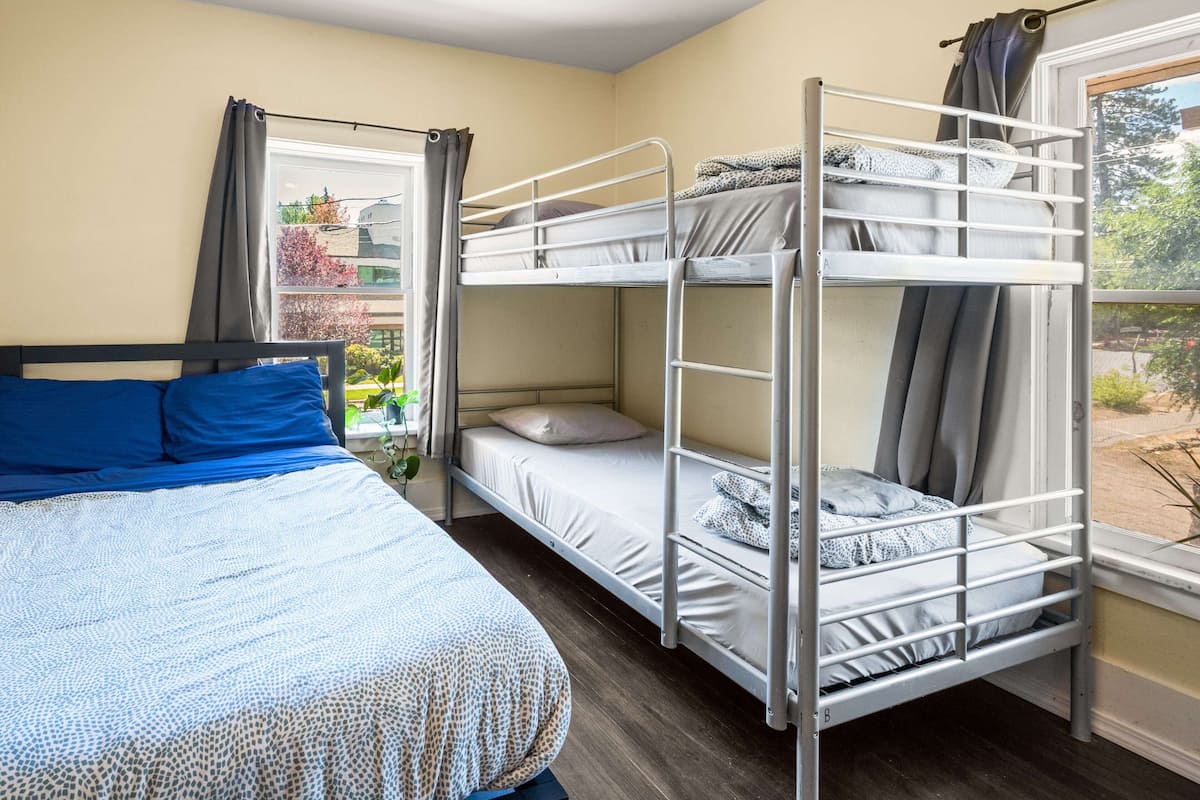 A dormitory room with bunk beds, a single bed, and a window with curtains.