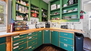 A kitchen with green cabinets, a wooden countertop, and various kitchen appliances and utensils. - Bunk+Brew Historic Lucas House - Hostel (Bend)