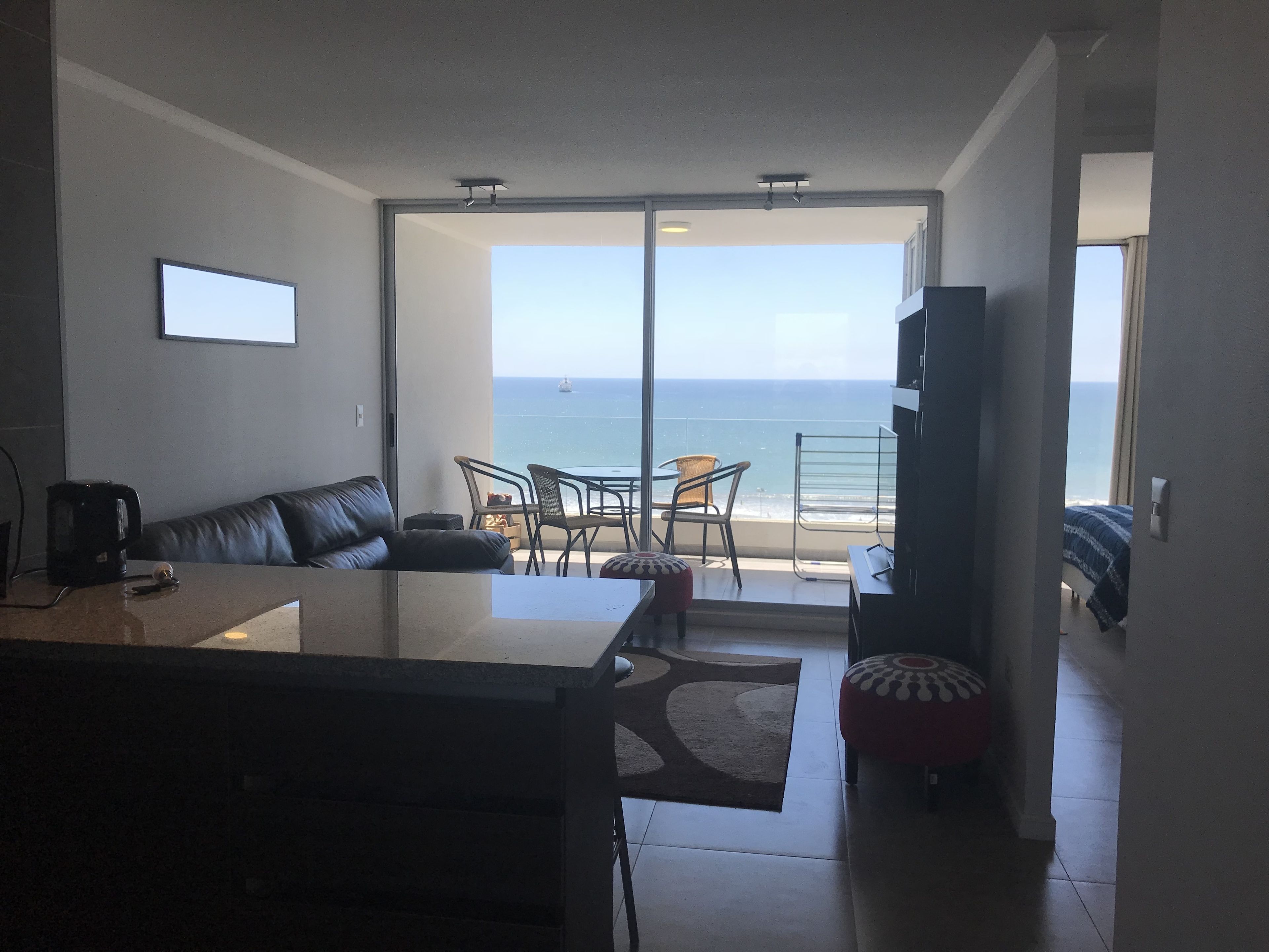 A modern living room with a sofa, coffee table, and a view of the ocean through large glass doors.